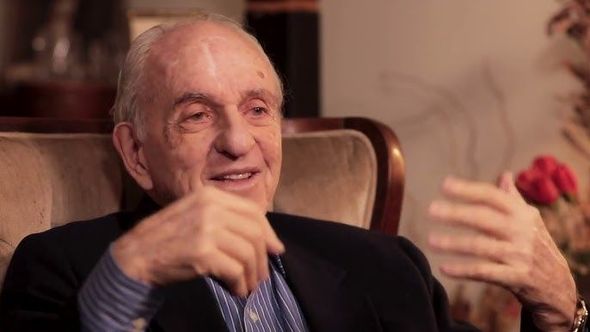 A man in a suit is sitting in a chair with his hands outstretched