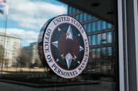 U.S. Office of Personnel Management seal on a glass door, reflecting buildings and sky