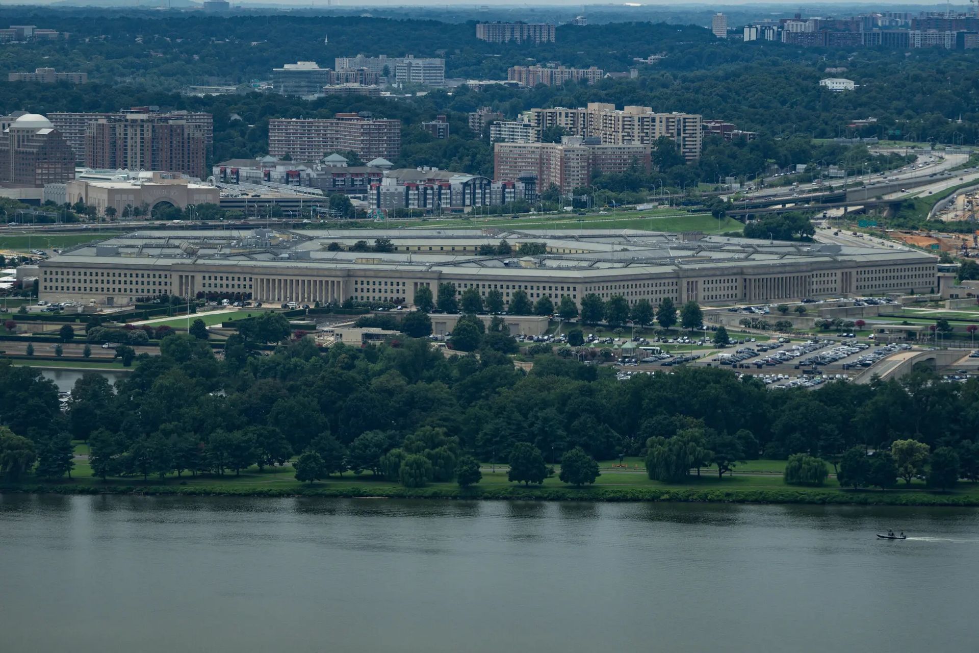 Aerial view of The Pentagon building in Arlington, Virginia, situated near a river with trees and surrounding cityscapes.