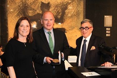 A man in a suit and tie is holding a medal while standing next to two women.