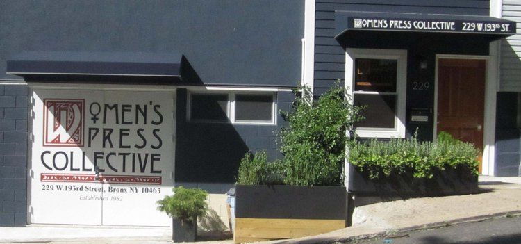 Exterior view of the Women's Press Collective storefront; blue building with black awnings, door and window.