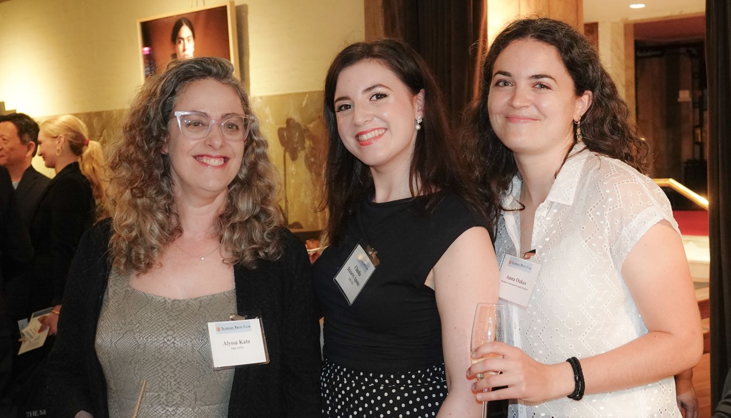 Three women posing for a picture with one wearing a name tag