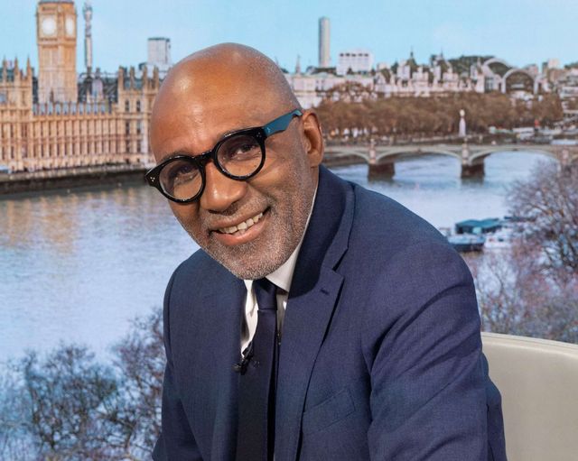 Smiling man in glasses and blue suit seated with London skyline and River Thames behind him