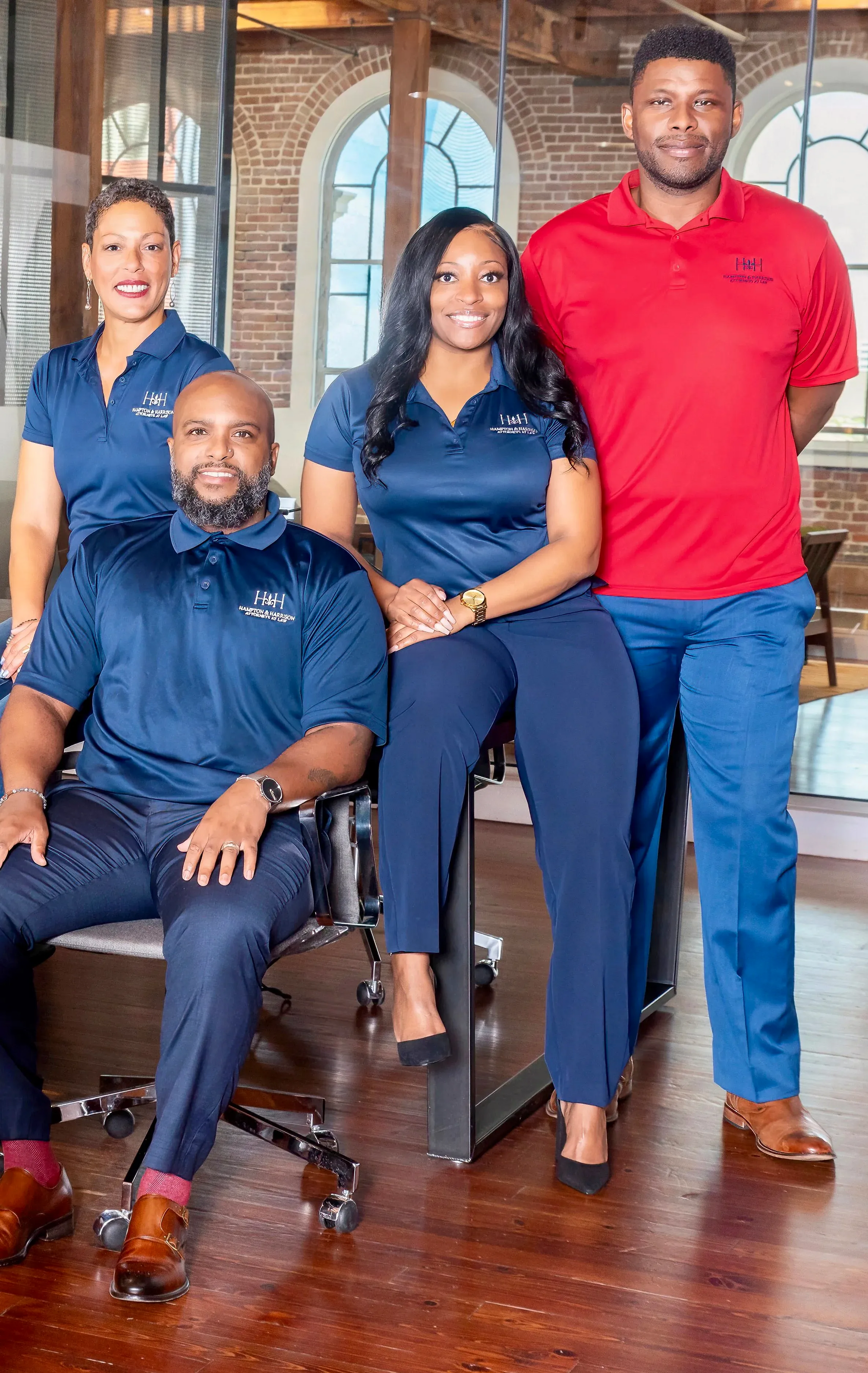Four people in business casual attire posing indoors. Two seated and two standing. Blue and red shirts.