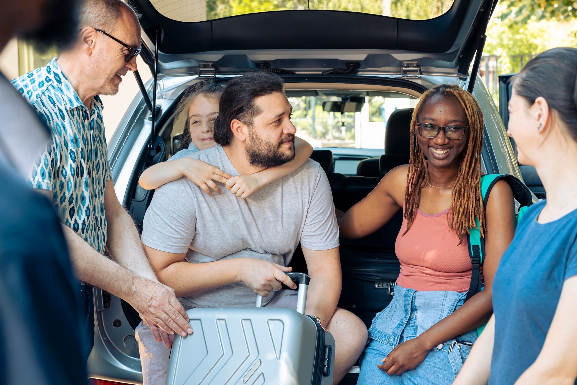 Family loading luggage into a car trunk; smiling people gather outdoors.