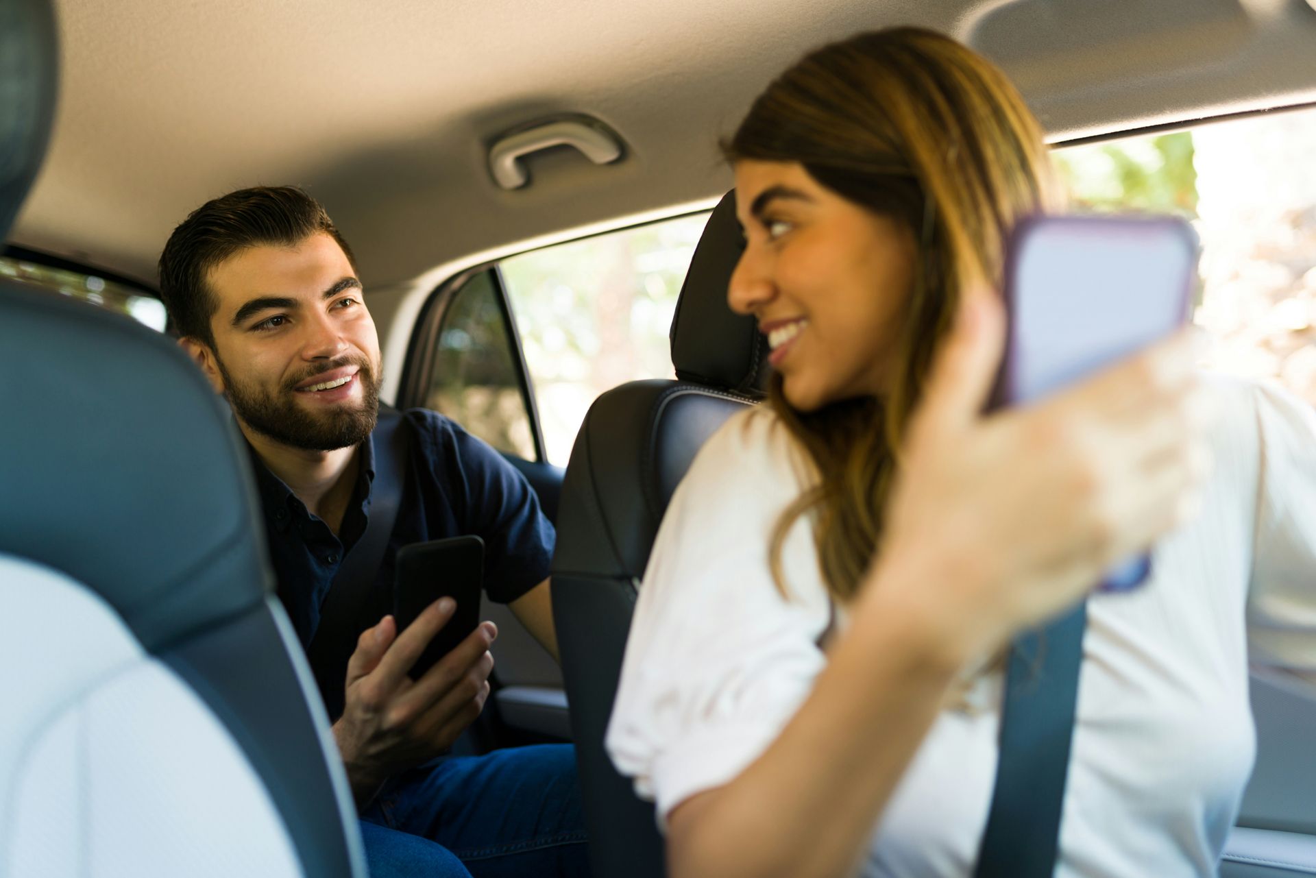 Woman takes a selfie with her phone while sitting in the backseat of a car with a man.