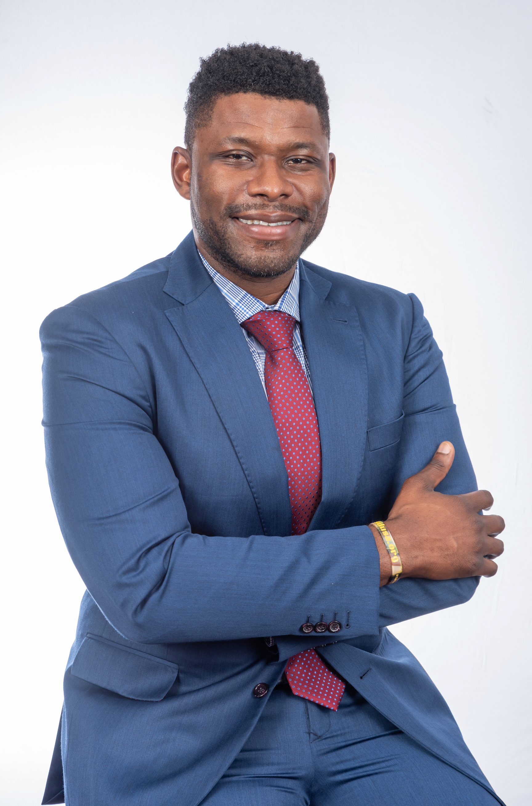 Man in blue suit, red tie, smiling with arms crossed against a white backdrop. 