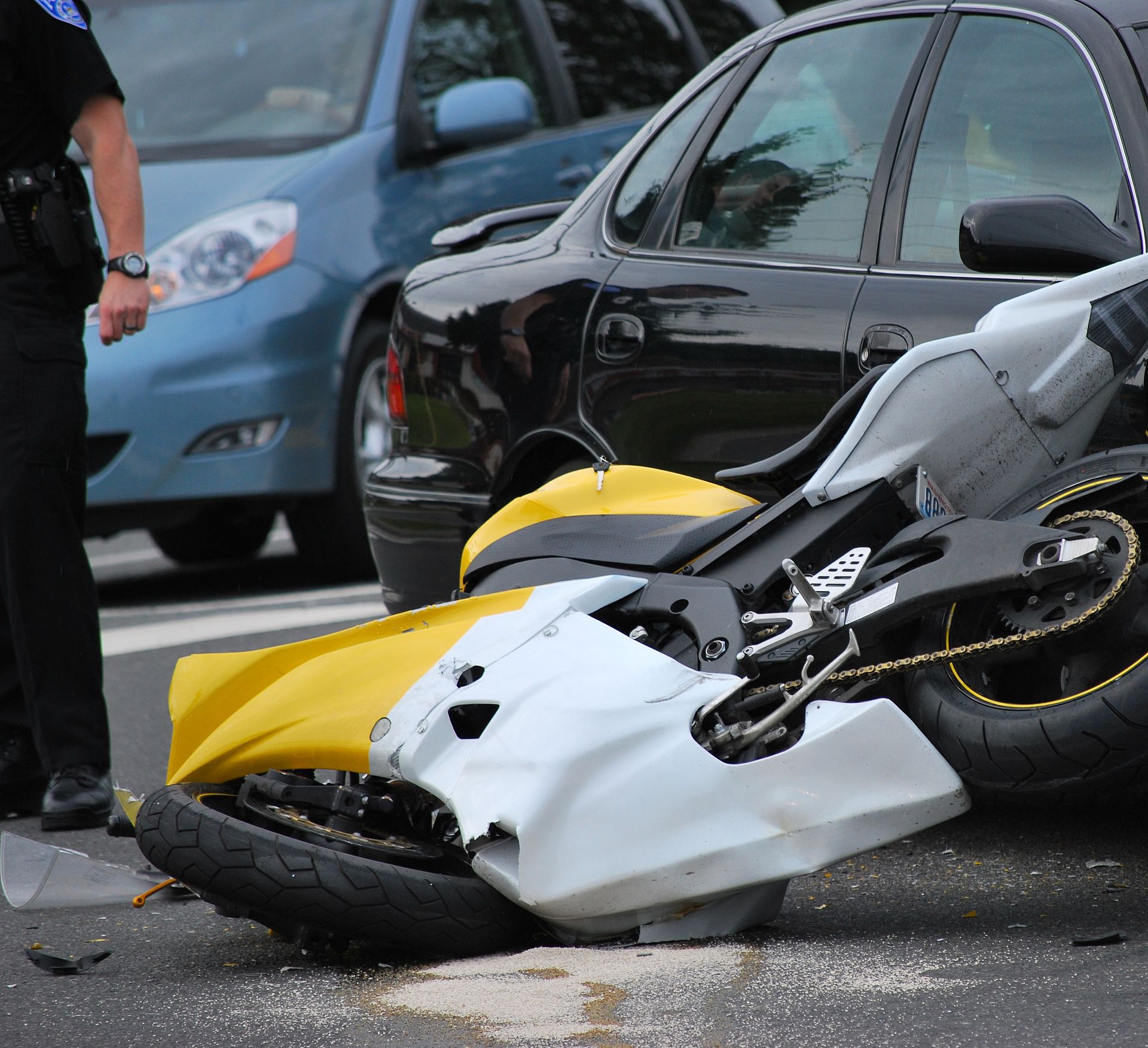 Motorcycle and two cars involved in a collision on a road. A police officer stands nearby.