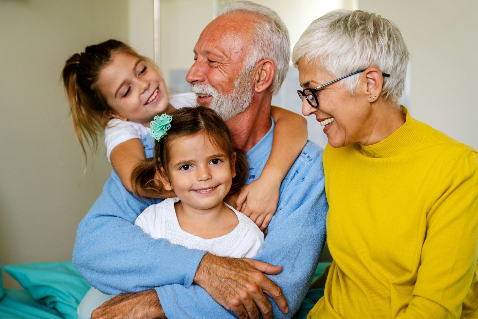 A man and woman are hugging two little girls while sitting on a bed.
