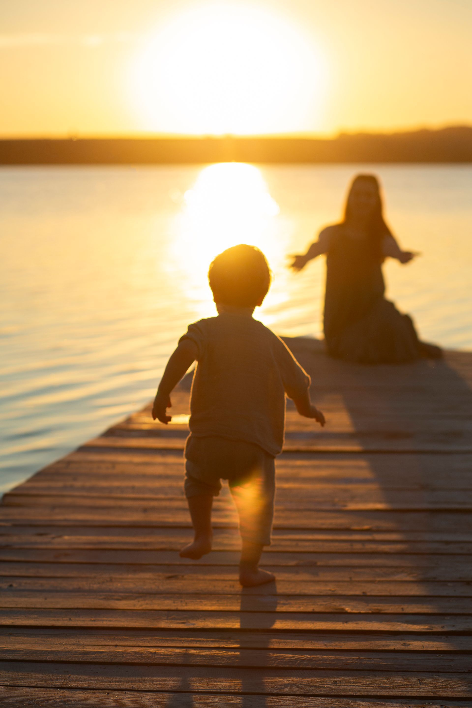 A baby is walking on a dock at sunset.