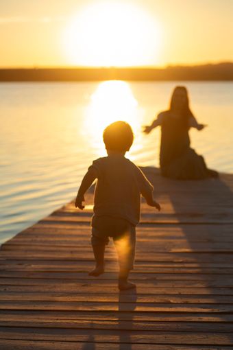 A baby is walking on a dock at sunset.