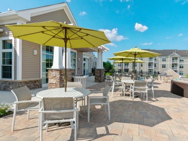 Gradient apartment community poolside lounge with seating area, tables, chairs, and green umbrellas.