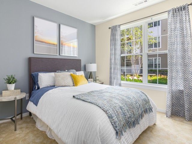 Gradient apartment bedroom with light blue wall, wall art, bed, and oversized window.
