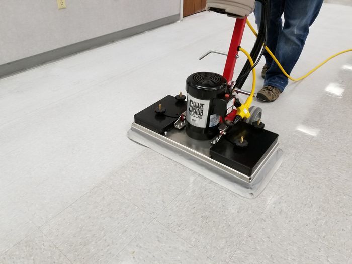 A person is using a machine to clean a white tile floor.