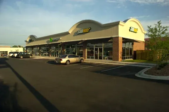 A subway restaurant with cars parked in front of it