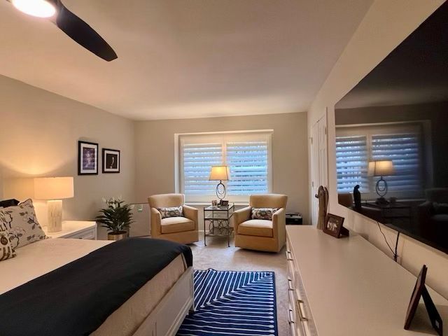 A bedroom with a bed , two chairs , a television and a ceiling fan.