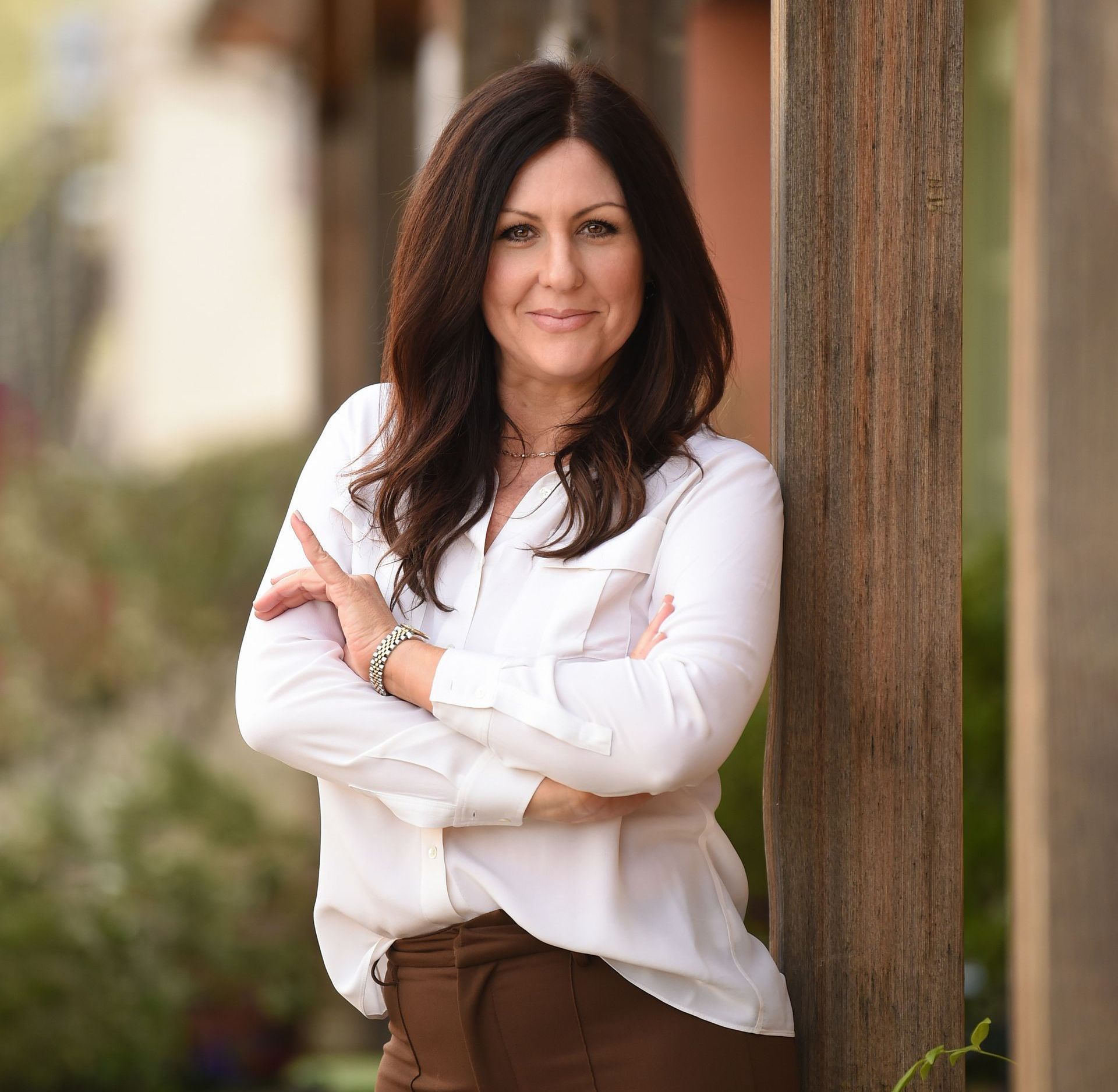 A woman is leaning against a wooden post with her arms crossed.