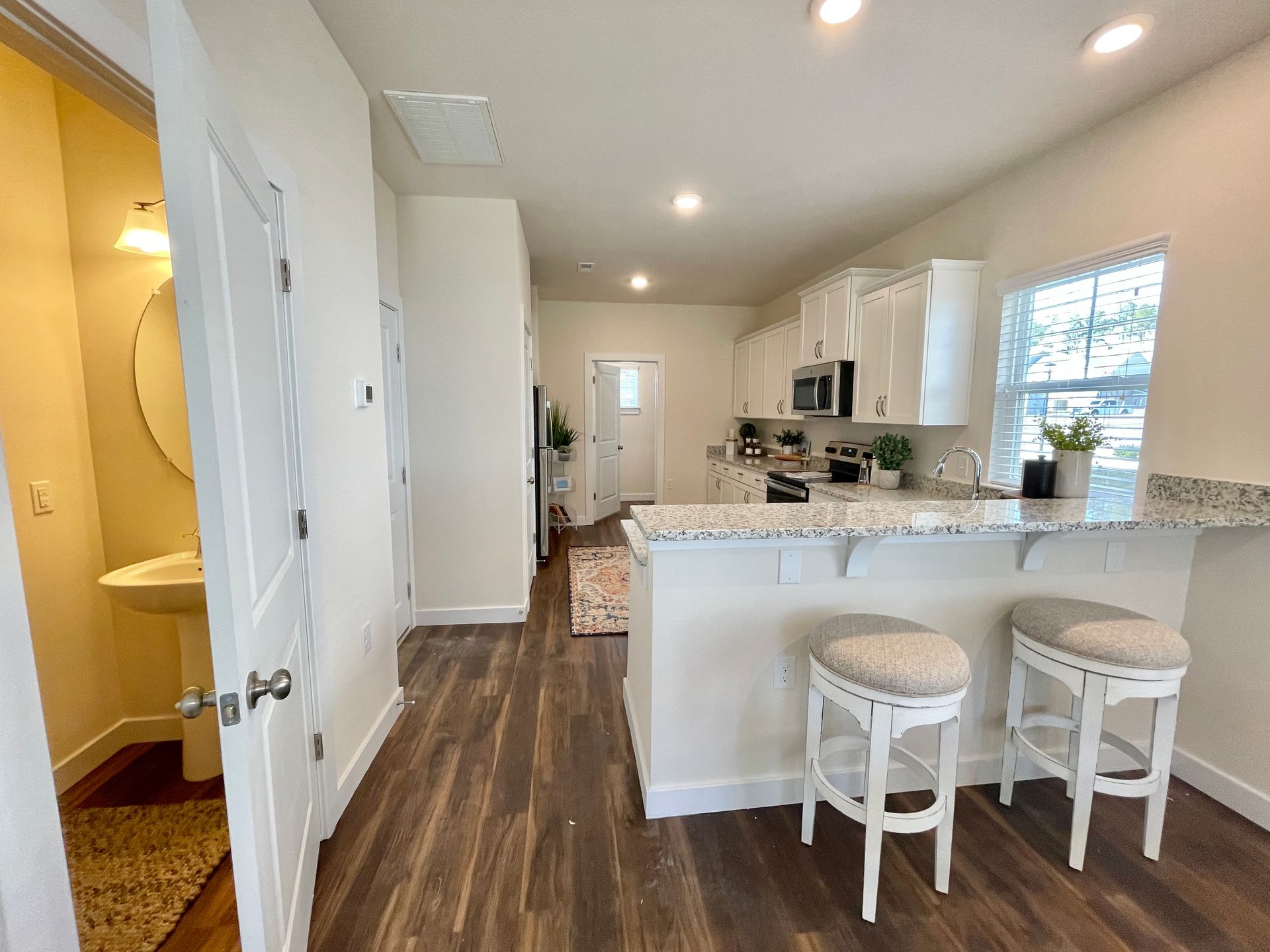 A kitchen with a bar and stools and a bathroom in the background.