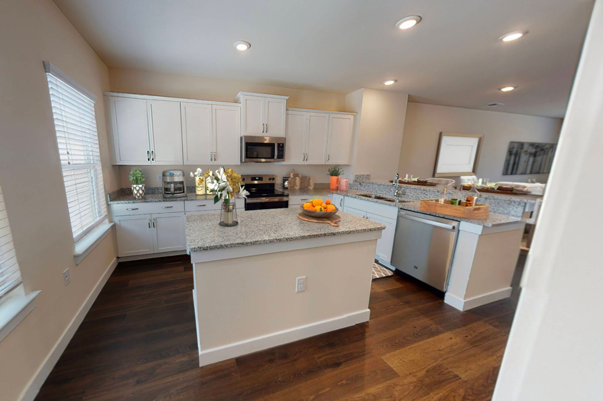 A kitchen with white cabinets , granite counter tops , stainless steel appliances , and hardwood floors.