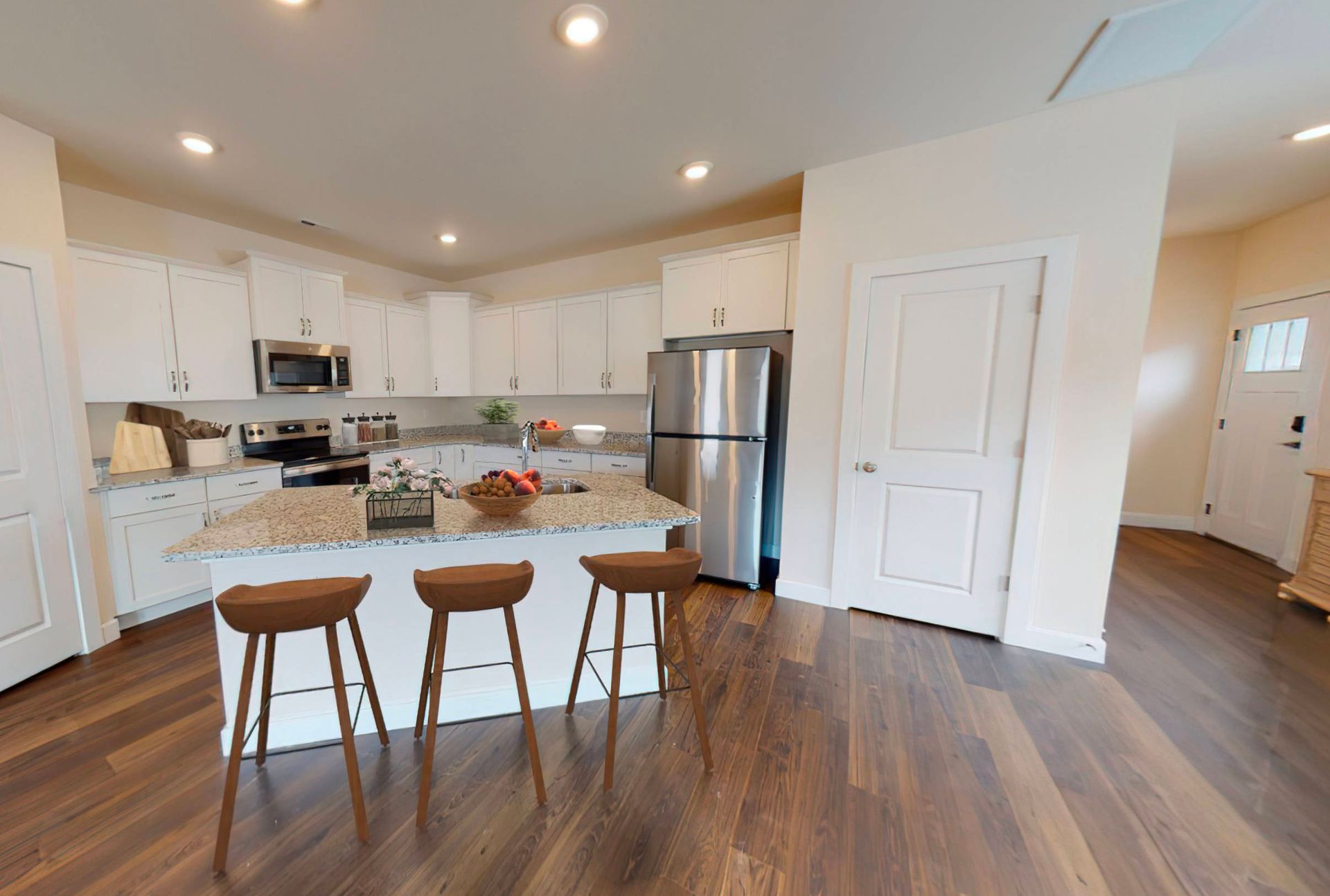 A kitchen with a large island , stools , a refrigerator , and a microwave.