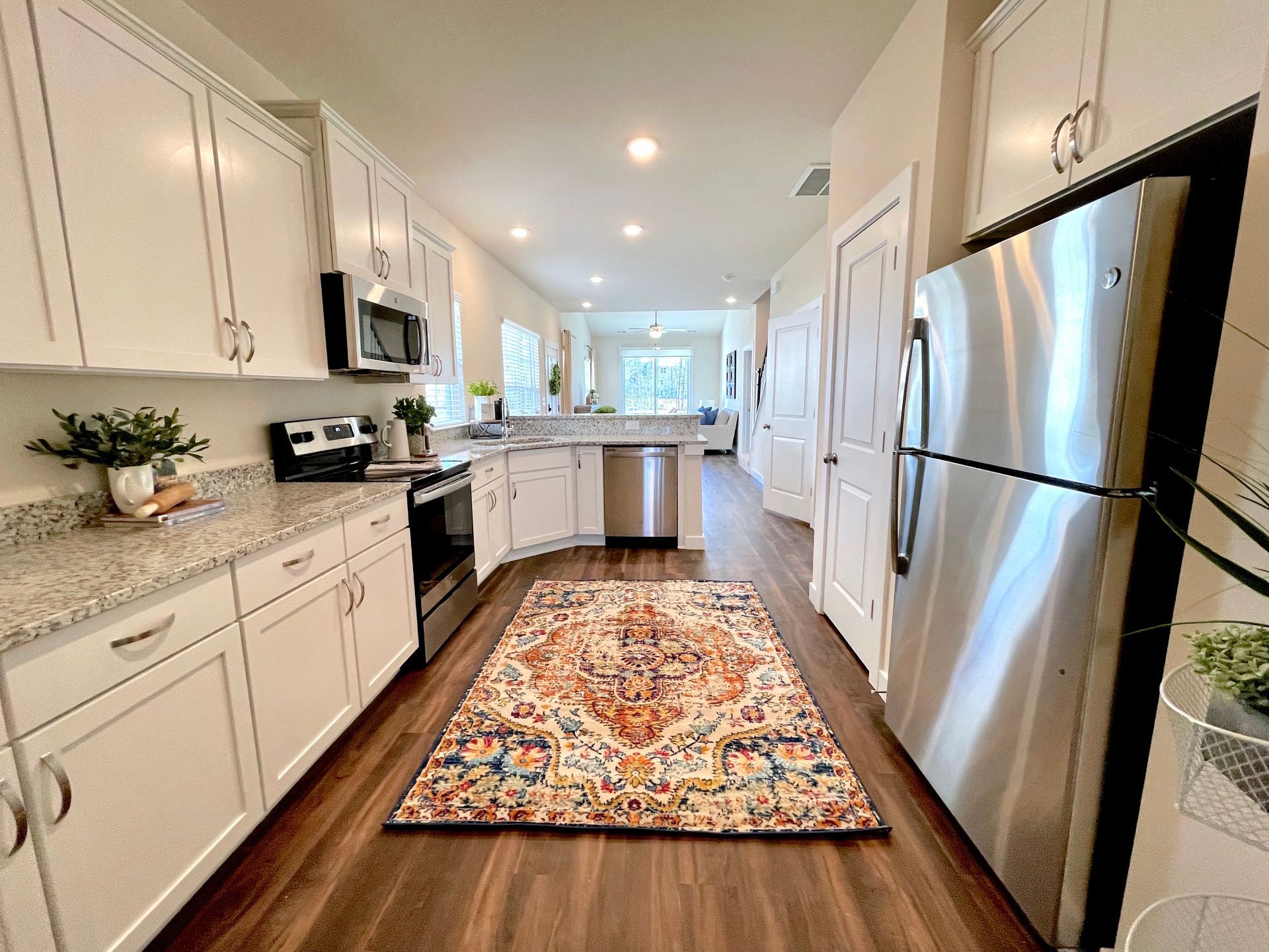 A kitchen with white cabinets and stainless steel appliances and a rug on the floor.