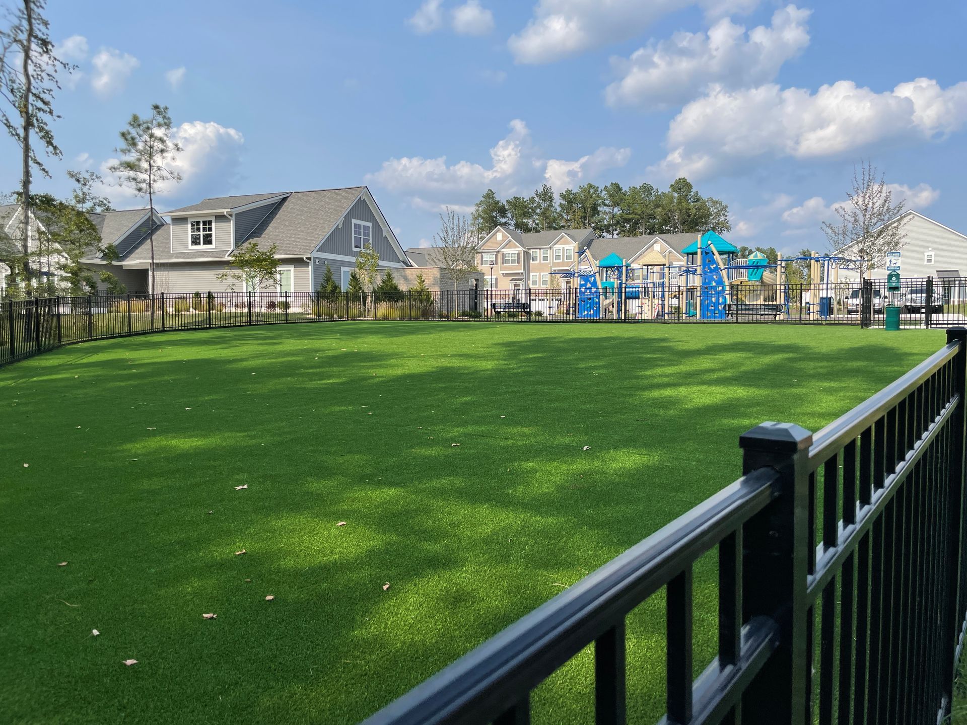 A fence surrounds a large grassy field with a playground in the background.