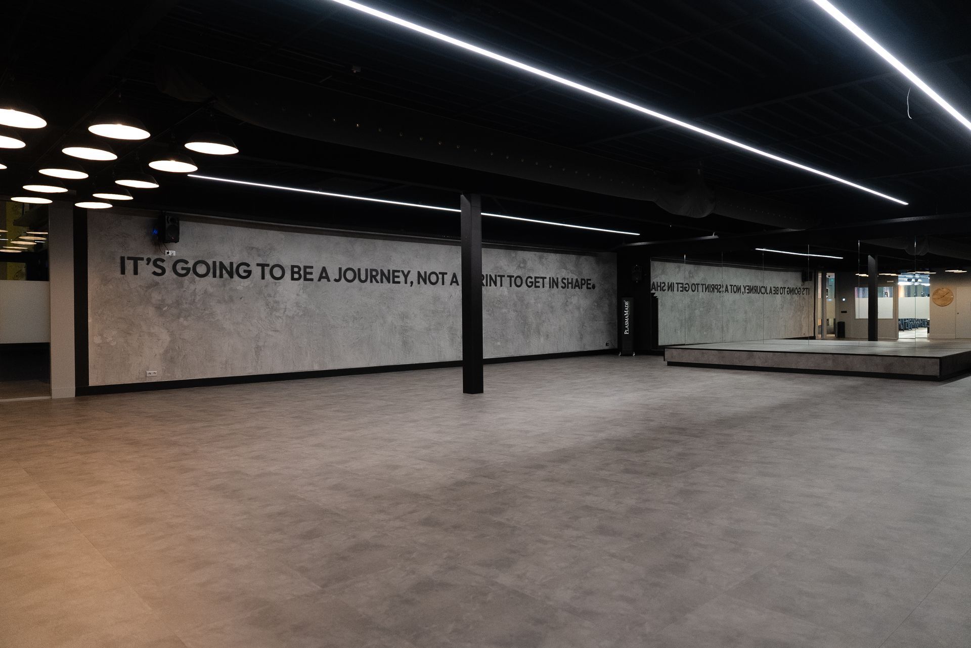 Een grote lege kamer met een muur waarop staat: 'Het wordt een reis, geen bestemming'.