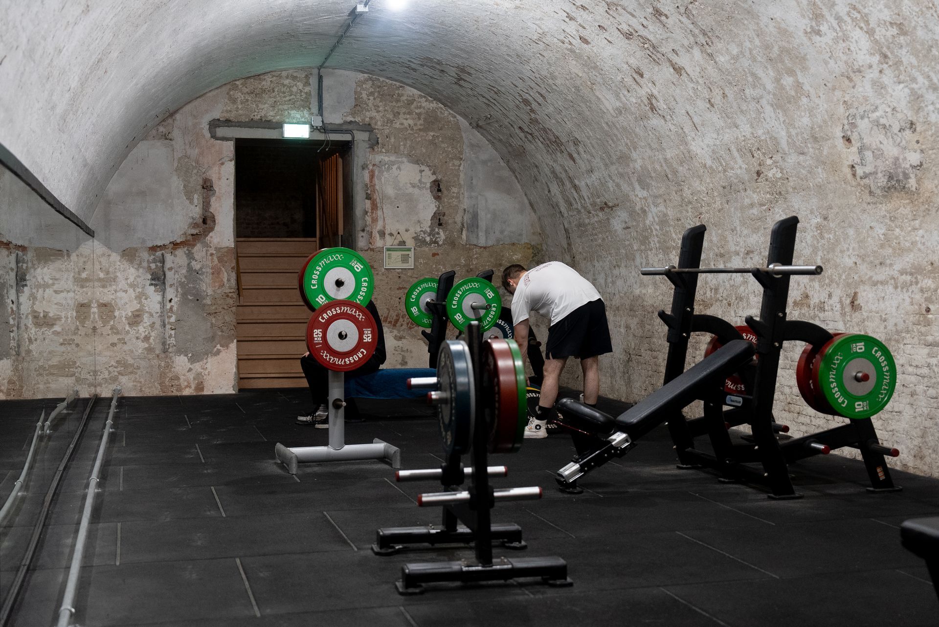 Een man hurkt op een bankje in een sportschool.