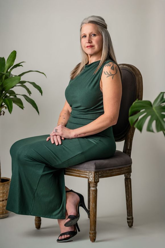A woman in a green dress is holding a pen and a painting.