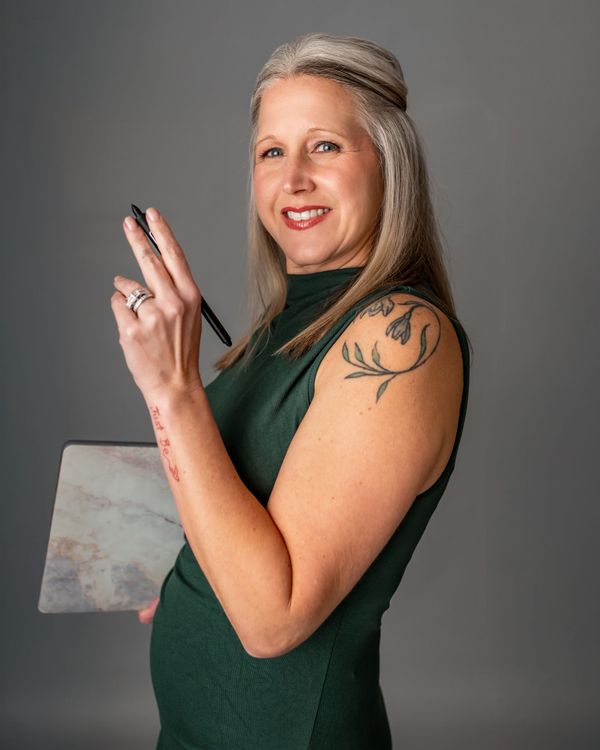 A woman in a green dress is holding a pen and a painting.