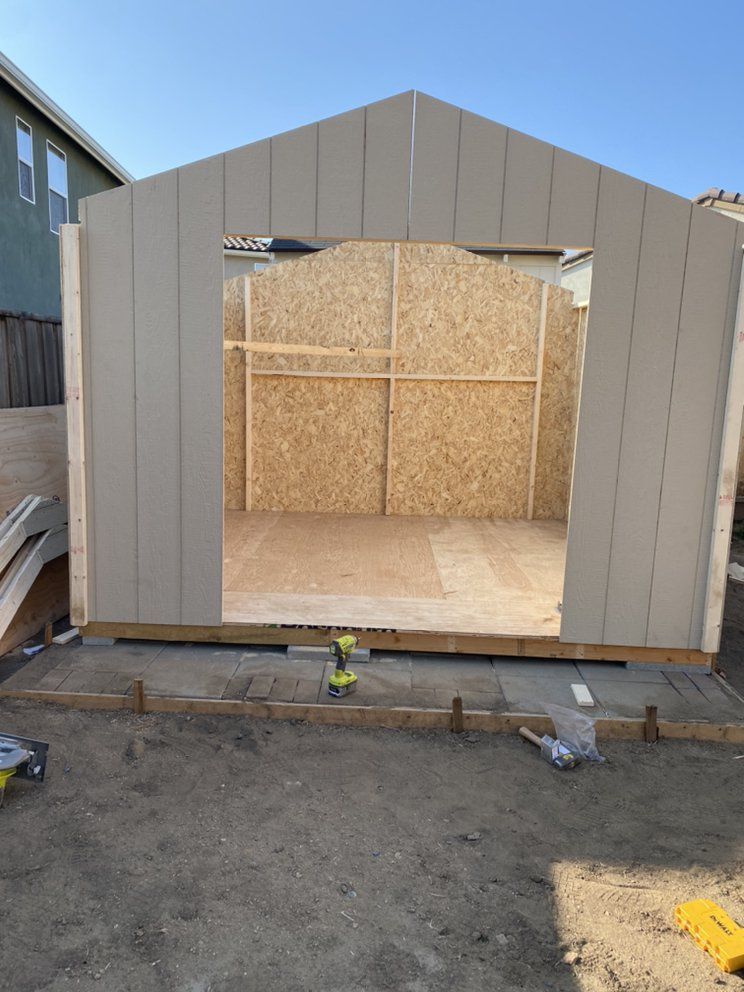 A shed is being built in a backyard with a drill on the ground.