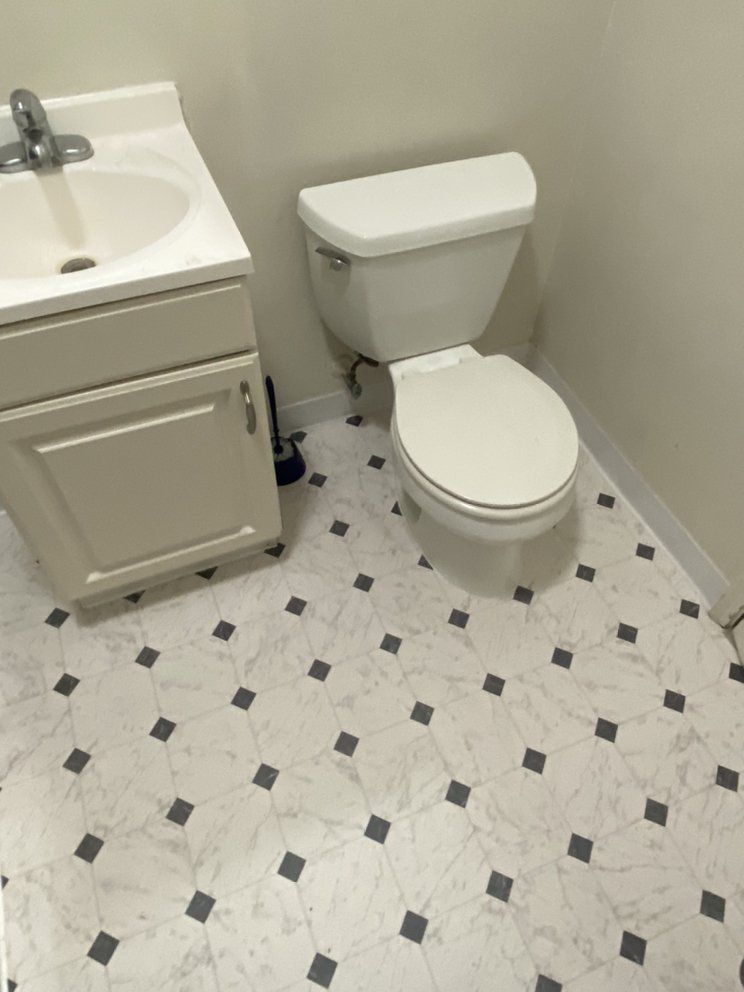 A bathroom with a toilet a sink and a black and white tile floor