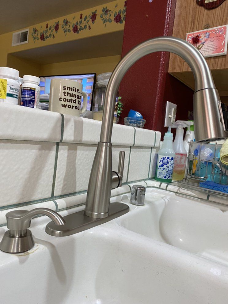 A kitchen sink with a stainless steel faucet and a bottle of soap on the counter.