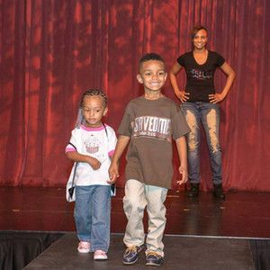 A boy and a girl are walking down a runway at a fashion show.