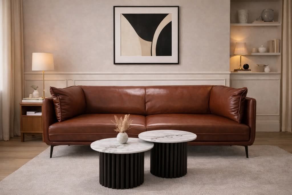 Sala de estar con sofá de cuero marrón, mesas con cubierta de mármol, arte abstracto y estanterías empotradas.