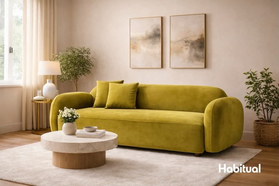 Sofá de terciopelo amarillo en una sala de estar con arte, una mesa de café y plantas.