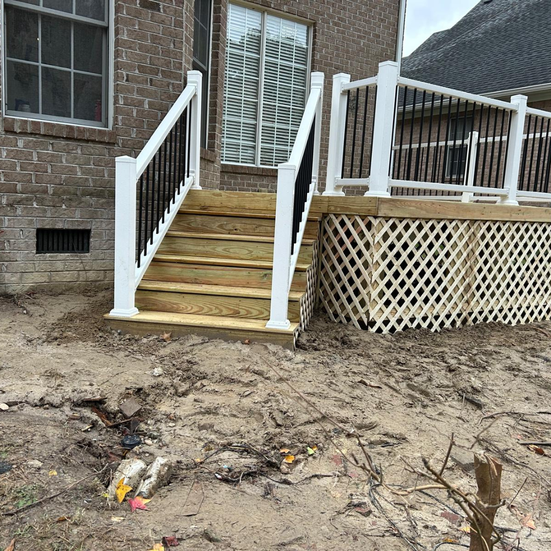 Wooden steps with black and white railing lead to a deck attached to a brick house.