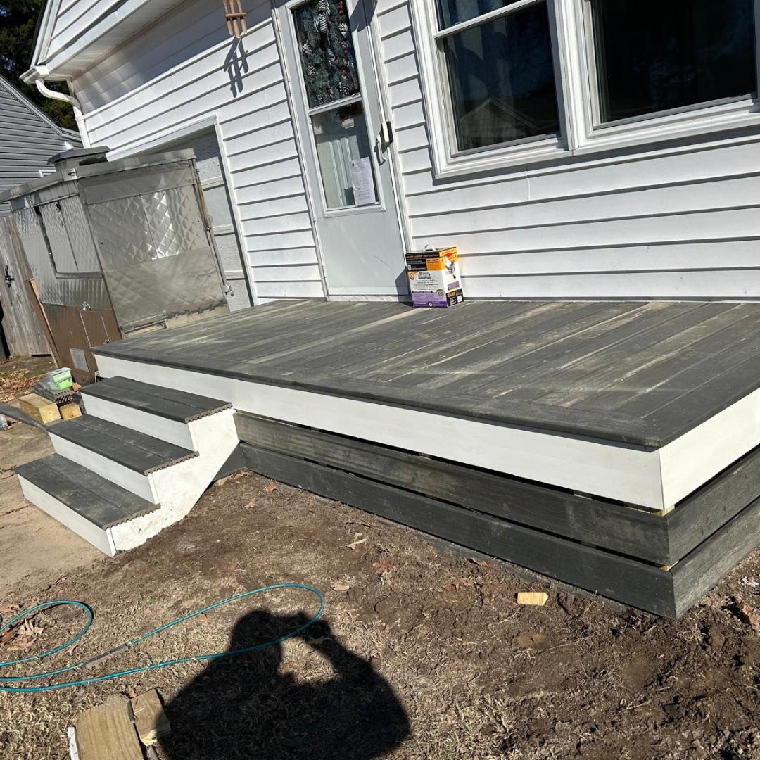 Deck with steps leading to a house door. Composite decking in gray and black, white trim.