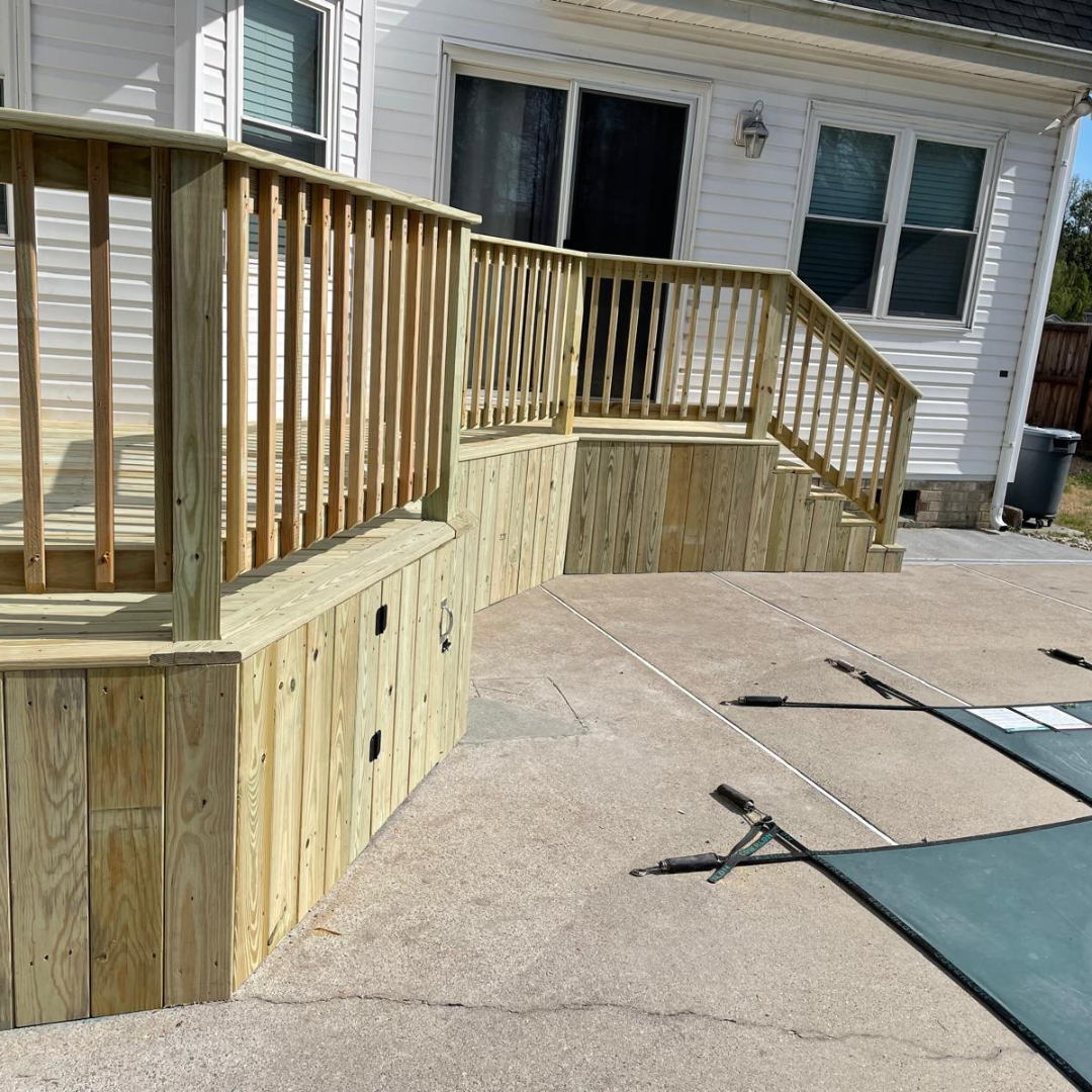 Wooden deck with railing, steps, and a concrete patio by a house.