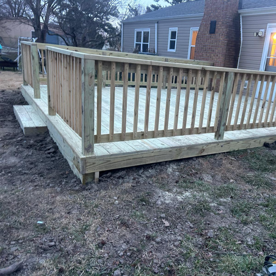 Newly constructed wooden deck with railing, beside a house, outdoors.