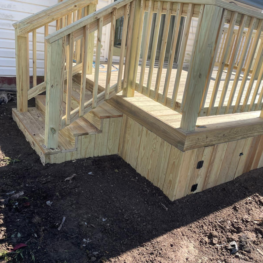 Wooden deck with stairs and railing attached to a house, built in the yard.