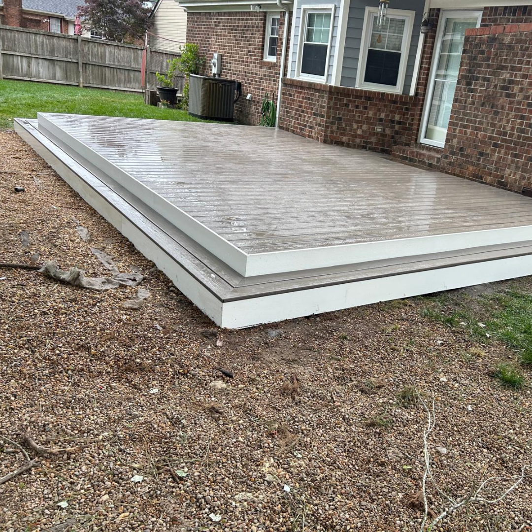 A two-tiered composite deck with white trim next to a brick house and a brown yard.