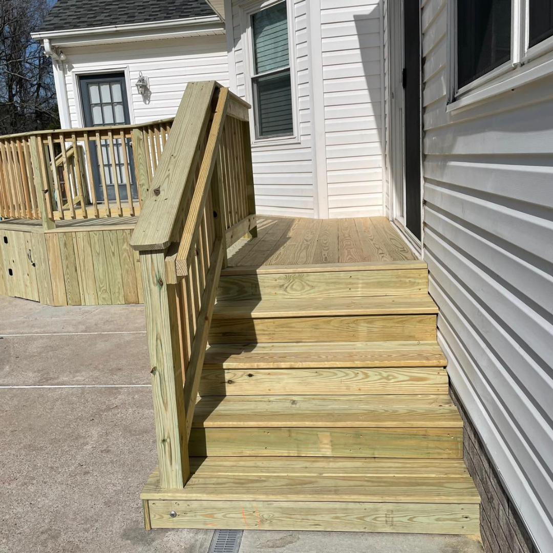 Wooden outdoor steps leading up to a doorway, with a railing and a deck in the background.