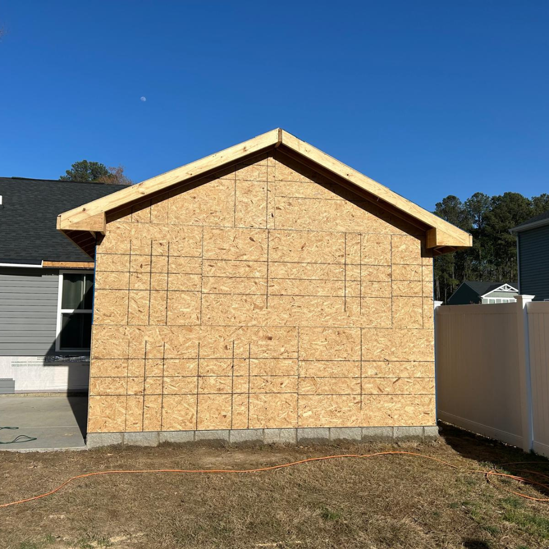 Construction of a shed, unfinished wood siding with a gabled roof, on a concrete foundation.