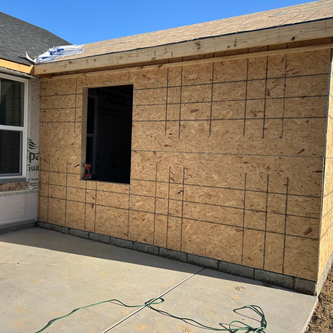 Exterior wall of a building under construction.  OSB paneling and a window frame are visible.