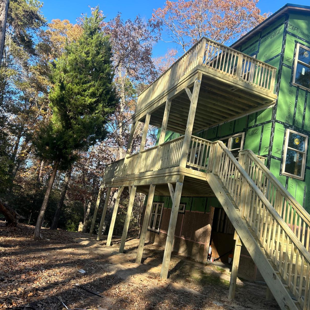 Wooden decks attached to a house with green siding; a stairway connects the decks to the ground.