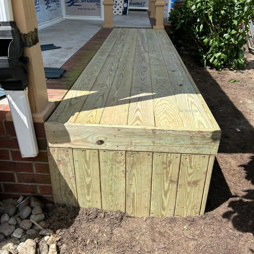 Wooden ramp with vertical slats, providing access to a brick porch, located outdoors.