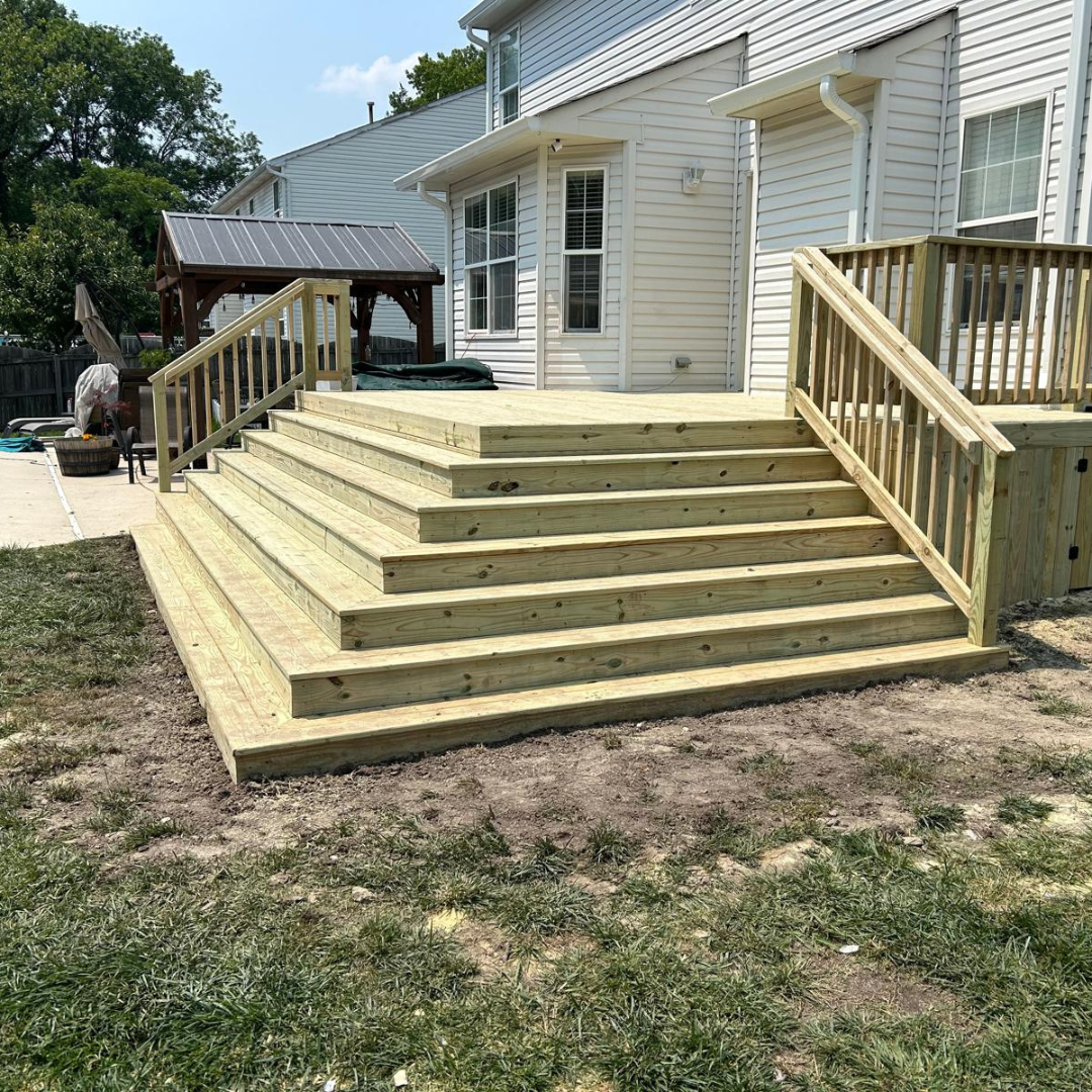 Wooden deck and steps leading to a house, with railings and a grassy yard.