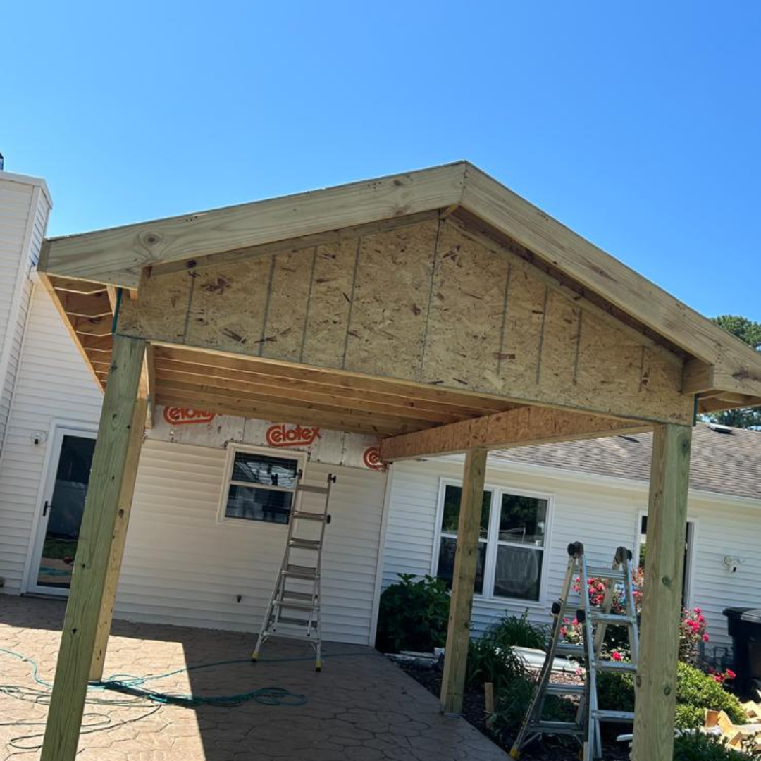 A partially built wooden patio cover attached to a white house on a sunny day.