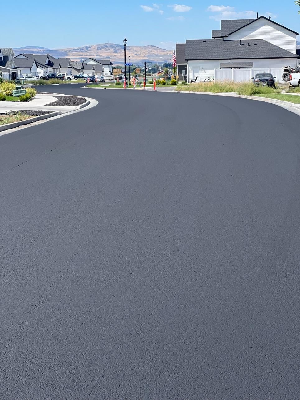 A black asphalt road in a residential area with houses in the background.